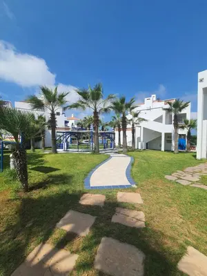 a walkway in a park with palm trees and a building at Passadena Village, Sidi Rahal in Sidi Rahal