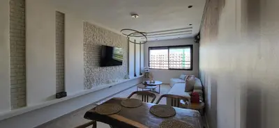 a living room with a table and a tv on a wall at Le Cocon d'Oasis - Location journalière Casablanca in Casablanca