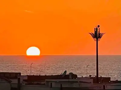 an orange sunset over the ocean with a street light at DreamParc - Vue sur Mer et Parc Securite 24H in Mohammedia