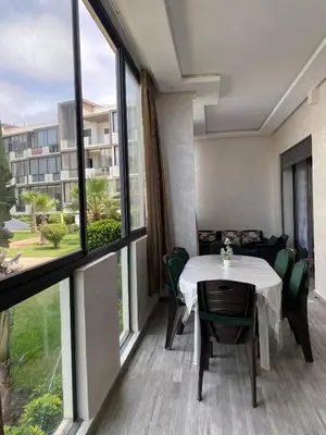 a room with a table and chairs and large windows at Appartement - Dar Bouazza spacieux avec piscine à Dar Bouazza in Dar Bouazza