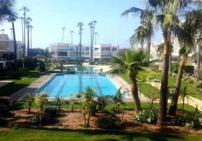a large swimming pool with palm trees and a building at Appartement meublé piscine Residence eden tamaris in Dar Bouazza