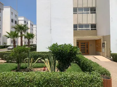 a building with bushes and trees in front of a building at La location de la mer in Dar Bouazza