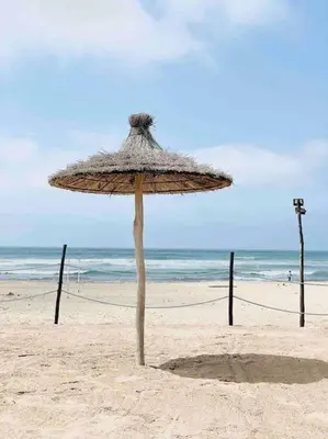 a straw umbrella sitting on a sandy beach at Appartement pieds dans l’eau Tamaris in Casablanca