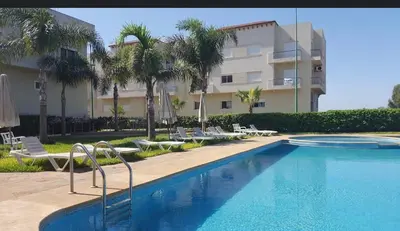a swimming pool with chairs and a building at OASIS BEACH APPARTEMENT MEUBLé RESIDENCE FERMÉE AVEC PISCINE TAMARIS 2 SIDI RAHAL in Sidi Rahal