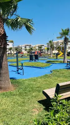 a park with a bench next to a palm tree at Residence Casa Bay Sidi Rahal in Sidi Rahal