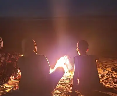 two people sitting around a fire at night at Sidi Rahal Blue View, Beachfront wide seaview with pool in Sidi Rahal