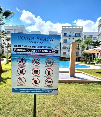 a sign in the grass in front of a resort at Idéal séjour Cozy aprt bouznika piscine et plage in Bouznika