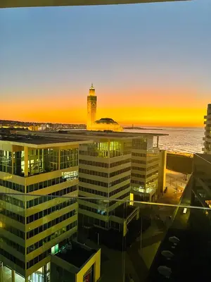 a view of a building and a lighthouse at sunset at Magnifique appartement pleine vue mer Marina Casablanca in Casablanca