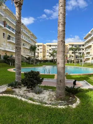a swimming pool with palm trees in front of a building at Bouznika Beach appartement de luxe avec piscine in Bouznika