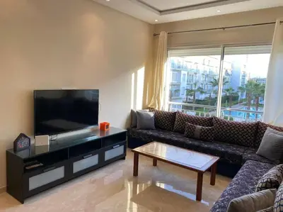 a living room with a couch and a flat screen tv at Jolie Appartement 2 chambres / vue piscine in Bouznika