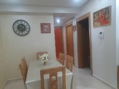 a dining room with a table and chairs and a clock at superbe appartement vue piscine in Bouznika