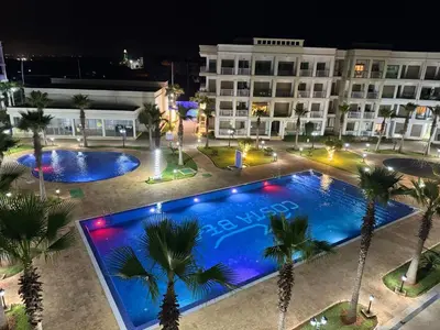 a hotel with two pools and palm trees at night at Douce escale vue sur piscine - Costa Beach bouznika in Bouznika