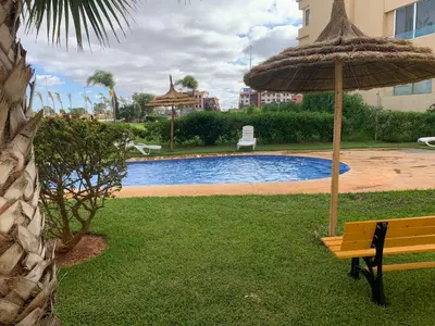 a bench with an umbrella next to a swimming pool at Appartement de luxe avec vue sur mer in Bouznika