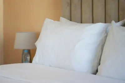 a bed with white pillows and a table with a lamp at Maison avec Piscine Proche Plage in El Harhoura