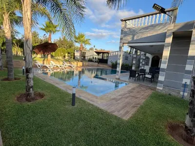 a pool with chairs and an umbrella next to a building at Villa Ines avec piscine privée in Sidi Moussa Ben Ali