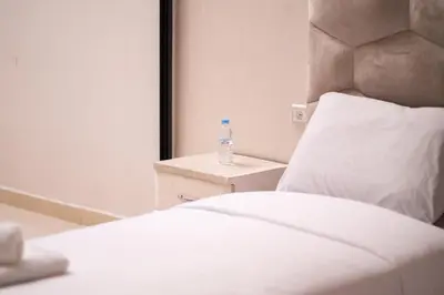 a white bed with a bottle of water on a table at Appartement Proche Plage in Bouznika