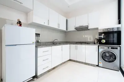 a kitchen with white cabinets and a washer and dryer at Appartement Proche Plage in Bouznika