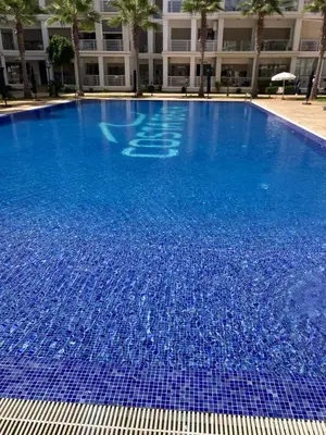 a large swimming pool with blue water in front of a building at Grand appartement vue sur piscine Bouznika in Kasba Bou Hamira