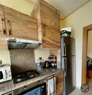 a kitchen with a stainless steel refrigerator and wooden cabinets at Appartement de vacances CASABAY Sidi Rehal in Sidi Rahal