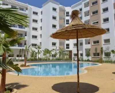 an umbrella and a swimming pool in front of a building at Family Appartement Nouaceur Aéroport Med V in Nouaceur
