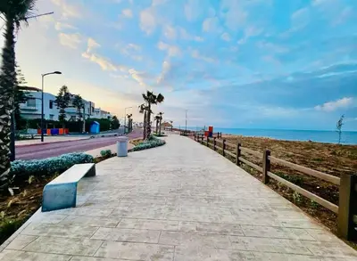 a sidewalk next to the beach with a bench at Confort Moderne à 2 Pas de la Mer Calme Absolu in Dar Bouazza
