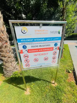 a sign in the grass next to a palm tree at Appartement Dahlia - Haut Standing - Mohammedia Natura Living in Mohammedia