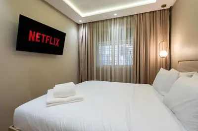 a bedroom with a white bed with a netflix sign on the wall at Appartement Élégant et Spacieux in LʼOasis