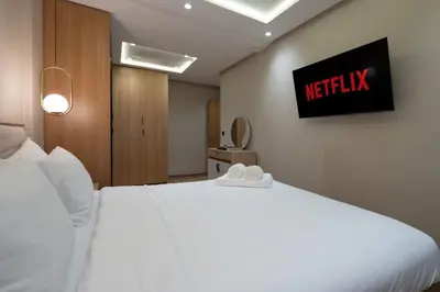 a white bed in a hotel room with a sign on the wall at Appartement Élégant et Spacieux in LʼOasis