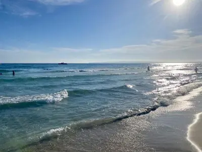 a beach with people swimming in the ocean at Bel Appartement avec Piscine et Jardin, EL MANSOURIA in Mansouria