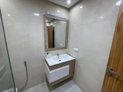 a white bathroom with a sink and a mirror at Garden Paradise Bouznika Beach Apartment in Bouznika