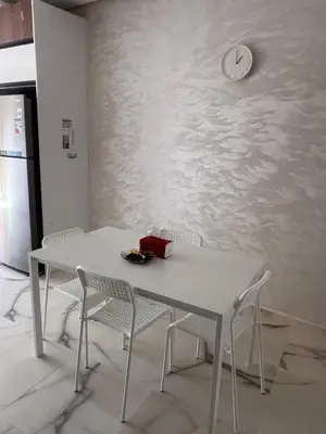 a white table and chairs with a clock on a wall at Bel appartement à louer sur bouznika de 117 m2 in Bouznika