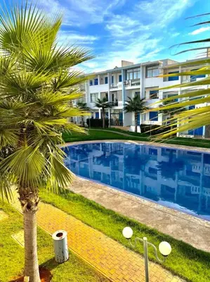 a palm tree and a building with a swimming pool at Bel Appartement vue piscine in Mansouria
