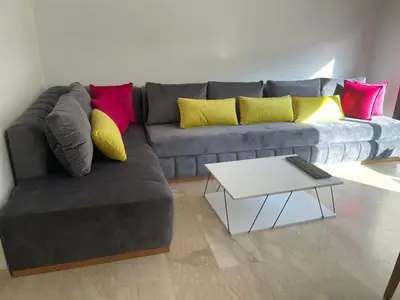 a living room with a gray couch with colorful pillows at Superbe Appartement pieds dans l'eau - Résidence GARDENBAY in Dar Mohammed Ould Haj Jilali