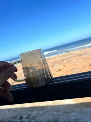 a person holding a drink in front of the beach at Appartement - EL Mansouria - Mohammadia - Bouznika in Mansouria