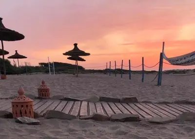 a sandy beach with umbrellas and a volleyball net at Superbe Appartement pieds dans l'eau Résidence Garden Bay in Sidi Rahal