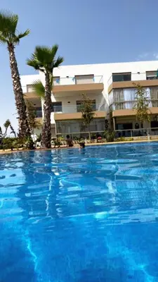a large swimming pool with palm trees in front of a building at Blue beach Sidi Rahal in Le Polo