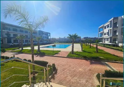 a courtyard with a pool and palm trees and buildings at Une petite parenthèse marine in Mansouria