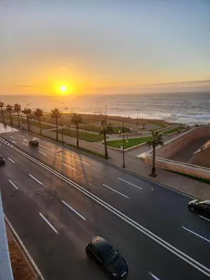 a road with cars on it with the ocean and the sunset at Joumaira appartement Beach in Rabat