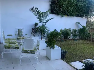 a patio with white chairs and plants in a yard at Melrose beach apartment in Tamaris