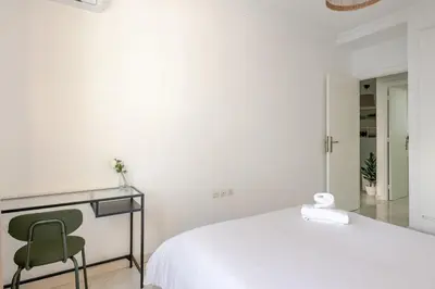 a white bedroom with a bed and a green chair at Rabat Centro Apartments in Rabat