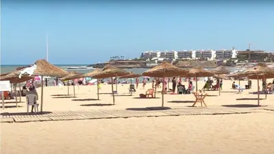 a beach with many straw umbrellas and people on it at Beautiful Apartment with Seaside Pool in Mansouria