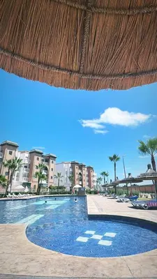 a swimming pool with a straw umbrella and some buildings at Al Kawtar in Mansouria