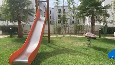 a playground with a slide in a park with palm trees at Appartement avec une Chambre, Salon, Salle de Bain et Piscine in El Harhoura