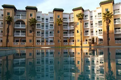 a building with palm trees and a reflection in the water at residence al kawtar in Mansouria