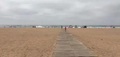 a person walking along a boardwalk on a beach at La perle de blanca beach in Sidi Rahal