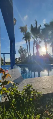 a view of a pool with palm trees and the sunset at Auberge Abrar in O Ben Slimane