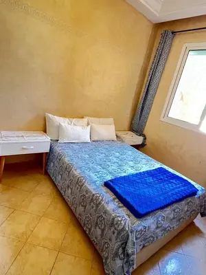 a bedroom with a bed with blue sheets and a window at Joli appartement Ricoflores El Mansouria in O Ben Slimane