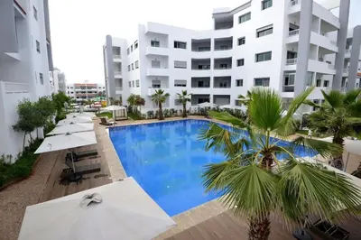 a swimming pool in front of a building with umbrellas at Luxury Beachview Apartment La siesta beach resort in Mohammedia