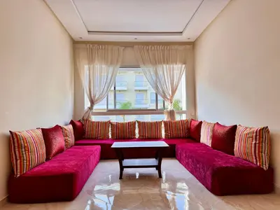 a red couch in a living room with a table at Bright Apt with Balcony, WiFi, Parking and Pool Resort in Bouznika