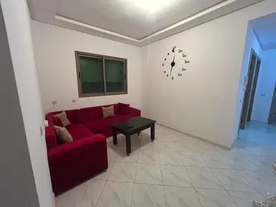 a living room with a red couch and a clock on the wall at Appartement meublé calme et chaleureuse in Temara